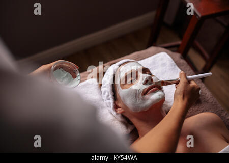Schöne Frauen, die eine Gesichtsmaske Behandlung im Spa von Therapeuten. Kosmetikerin, die Gesichtsmaske auf weibliche Gesicht. Stockfoto