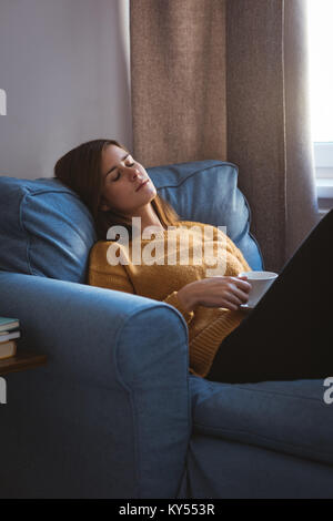 Junge Frau entspannt auf einem Sofa mit einer Tasse Kaffee im Wohnzimmer Stockfoto