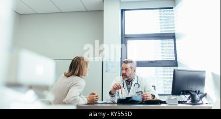 Männliche Arzt im Gespräch mit einem Patienten während der Anhörung in seinem Büro. Reifen Arzt erklären Diagnose zu den weiblichen Patienten. Stockfoto
