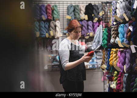 Frau auf der Suche nach Garn während der Verwendung digitaler Tablet Stockfoto