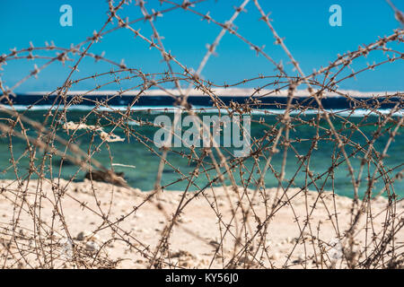 Alten Stacheldraht infront von Meer. Kabel und blauem Himmel mit Wolken. Schutzzaun von Stacheldraht gegen den blauen Himmel und das Meer. Close-up. Stockfoto