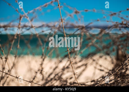 Alten Stacheldraht infront von Meer. Kabel und blauem Himmel mit Wolken. Schutzzaun von Stacheldraht gegen den blauen Himmel und das Meer. Close-up. Stockfoto