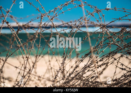 Alten Stacheldraht infront von Meer. Kabel und blauem Himmel mit Wolken. Schutzzaun von Stacheldraht gegen den blauen Himmel und das Meer. Close-up. Stockfoto