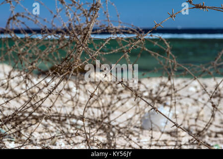 Alten Stacheldraht infront von Meer. Kabel und blauem Himmel mit Wolken. Schutzzaun von Stacheldraht gegen den blauen Himmel und das Meer. Close-up. Stockfoto