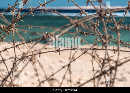 Alten Stacheldraht infront von Meer. Kabel und blauem Himmel mit Wolken. Schutzzaun von Stacheldraht gegen den blauen Himmel und das Meer. Close-up. Stockfoto