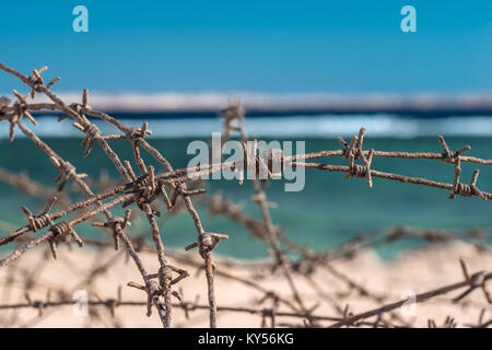 Alten Stacheldraht infront von Meer. Kabel und blauem Himmel mit Wolken. Schutzzaun von Stacheldraht gegen den blauen Himmel und das Meer. Close-up. Stockfoto