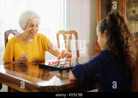 Glückliche kleine Mädchen spielen Checkers mit älteren Frau zu Hause. Familie Beziehung mit Großmutter und Enkelin. Oma und Enkel wi Stockfoto