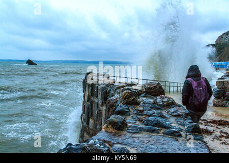 Einem Zuschauer bei nassem Wetter Zahnrad Uhren die Wellen gegen die Kaimauer am Meadfoot Beach in Paignton, Torbay, Devon, Großbritannien. Januar 2018. Stockfoto