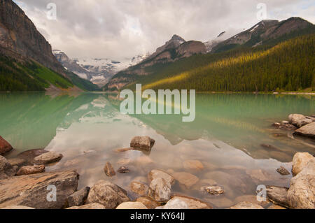 Erste Sonnenstrahlen, goldenes Sonnenlicht auf den Bergen am Lake Louise mit friedlichen Reflexionen. Stockfoto