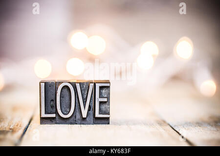 Das Wort Liebe in vintage Metall buchdruck Art auf einem bokeh Licht und Holz- Hintergrund geschrieben. Stockfoto