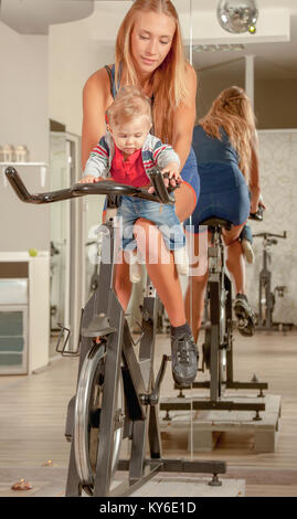 Junge schöne Mutter umarmt ihren niedlichen kleinen Jungen mit Zuneigung in einer Radfahren Fitnessstudio. Stockfoto