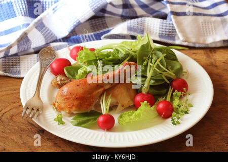 Gegrillte Hähnchenkeulen mit frischem Gemüse auf Holztisch auf weiße Platte serviert. Abendessen Hintergrund Stockfoto