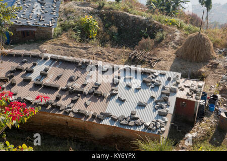 Wellblech Dach von einfachen Wohnungen mit großen Steinen, in Sarankot, Nepal gehalten Stockfoto