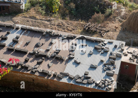 Wellblech Dach von einfachen Wohnungen mit großen Steinen, in Sarankot, Nepal gehalten Stockfoto