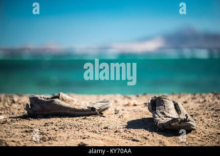 Paar alte schäbige Schuhe auf dem Sandstrand. Alten schäbigen Schuhe auf den Sand. Stockfoto