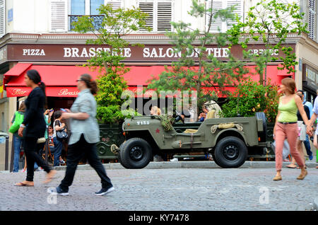 Die Brasserie Salons de thé im Pariser Viertel Montmartre, Frankreich mit amerikanischem Jeep aus Kriegszeiten. Leute, die vorbeilaufen Stockfoto