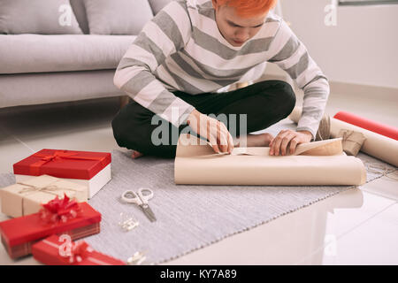 Junge glücklicher Mann Verpackung Valentine Geschenk beim Sitzen auf dem Boden Stockfoto