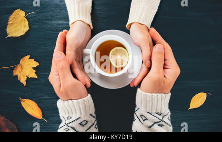 Paar Mann und Frau in Liebe Hände mit heißem Tee Zitrone Schale auf dunklen Holztisch mit Blätter im Herbst romantische Beziehung Gefühle Konzept top v Stockfoto