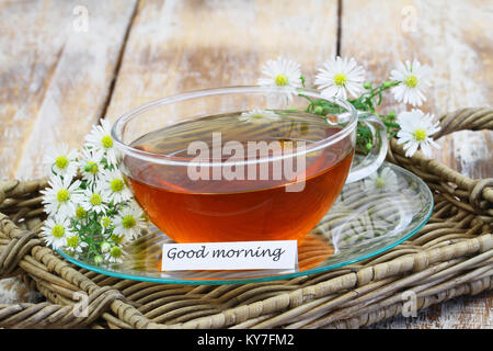 Guten Morgen Karte mit Kamillentee in transparenten Schale mit frischen Kamillenblüten Stockfoto