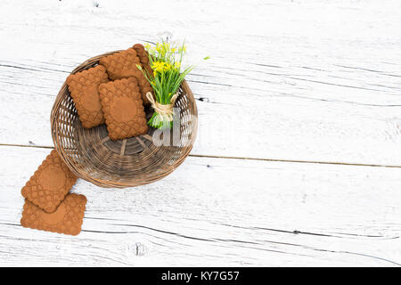 Korb mit Cookies und ein paar kleine gelbe Blumen auf weißem Holz- Hintergrund verschwommen. top View Stockfoto