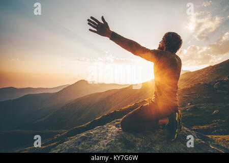 Mann bei Sonnenuntergang in den Bergen Beten erhobenen Händen Reisen Lifestyle geistige Entspannung emotionale Konzept Ferien im Einklang mit der Natur Landschaft Stockfoto