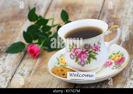 Karte Willkommen bei einer Tasse Tee in vintage Porzellan, Cookie und rosa Rose Stockfoto