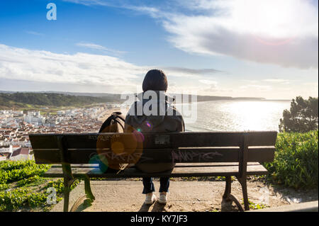 Frau sitzen auf einer Bank mit Blick auf die Küste und die Stadt von Nazare, Portugal. Stockfoto