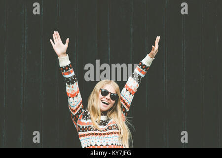 Lachende Frau happy hands up erhöht wellness Lifestyle Mode emotionale Mädchen mit gemütlichen Pullover gegen Holz- schwarzer Hintergrund Stockfoto