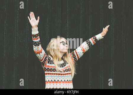 Junge Frau glücklich lächelnde erhobenen Händen Lifestyle Mode emotionale Mädchen mit gemütlichen Pullover gegen Holz- schwarzer Hintergrund Stockfoto