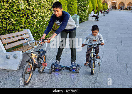 Isfahan, Iran - 23. April 2017: Zwei Brüder reiten Fahrräder und elektrische Skateboard auf dem Platz Naghshe Jahan. Stockfoto