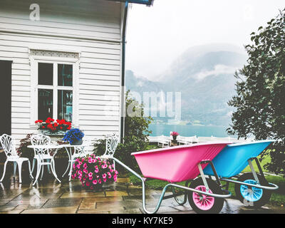 Gemütliche Landhaus Außenbereich Terrasse mit Blumen, Tisch und bunten Garten Trolley auf die Berge Stockfoto