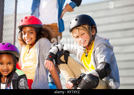 Portrait von jugendlichen Jungen in Roller Helm und Schutzausrüstung im Stadion mit Freunden im Freien sitzen, an der Kamera auf der Suche Stockfoto