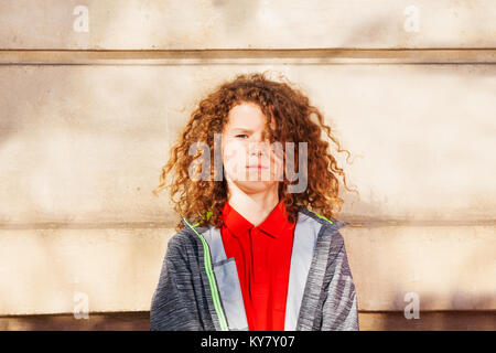 Portrait von Teenage curly schwarzhaarige Junge stehend gegen die Wand draußen und Suchen an Kamera Stockfoto