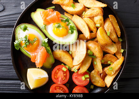 Avocado gefüllt mit Ei und Lachs, frische Tomaten und Frittierte Kartoffelecken auf einer Platte close-up. horizontal oben Ansicht von oben Stockfoto