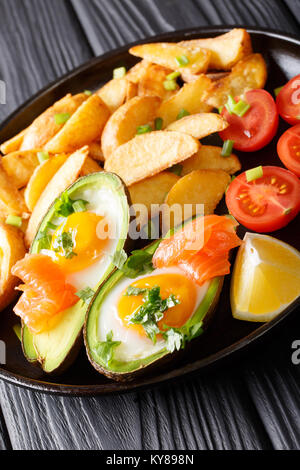 Gebackene Avocado gefüllt mit Ei und Lachs, frische Tomaten und gebratene Kartoffelscheiben closeup auf dem Teller auf dem Tisch. Vertikale Stockfoto