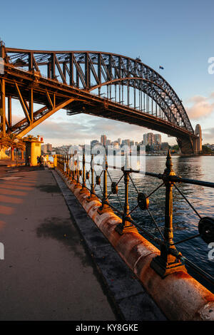 Bild vertikal der Sydney Harbour Bridge in Sydney, Australien, bei Sonnenaufgang von Hickson Road Reserve mit North Sydney und Luna Park im Hintergrund. Stockfoto