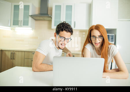 Erstaunt Paar mit offenen Mund auf Linie mit Laptop im Wohnzimmer im Haus Stockfoto