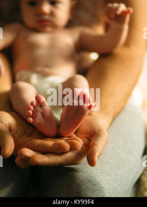 Neugeborenes Baby Beine in Mütter schöne Hand mit weichen Fokus auf und Schuhen Fuß Stockfoto