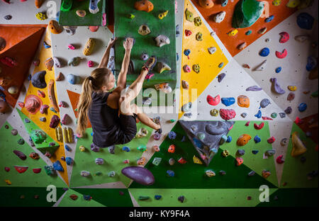 Junge Frau Bouldern auf überhängenden Wand in der Kletterhalle Stockfoto