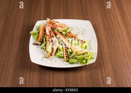 Octopus mit Zitrone und Salat auf einem weißen Teller Stockfoto