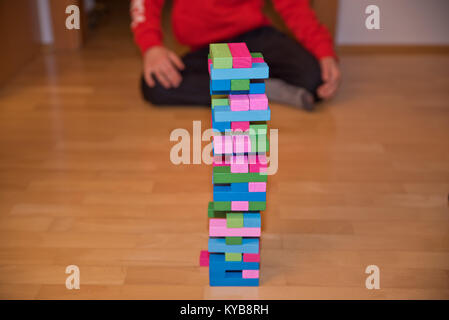 Kind hinter bunten Jenga tower aka Klodsmajor Gesellschaftsspiel sitzen, ein soziales Spiel, in dem Sie ein Turm aus Holz- Komponenten, bis er bricht zusammen Stockfoto