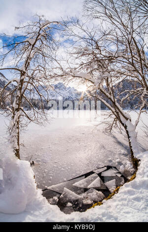 Gebrochene Eis auf dem See Fusine mit Berg Mangart und Sunbeam im Hintergrund Stockfoto