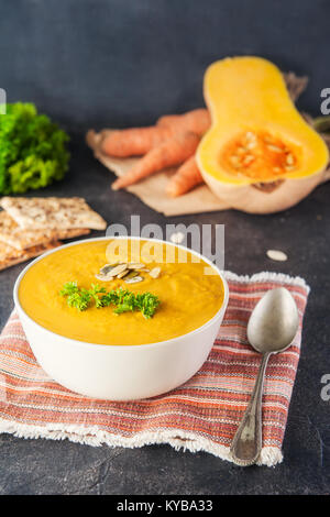 Schüssel aus gerösteten Kürbis und Karotten Cremesuppe mit Petersilie und Kürbis Samen auf dem dunklen Stein serviert Tabelle mit Zutaten. Selektiver Fokus, Kopieren sp Stockfoto