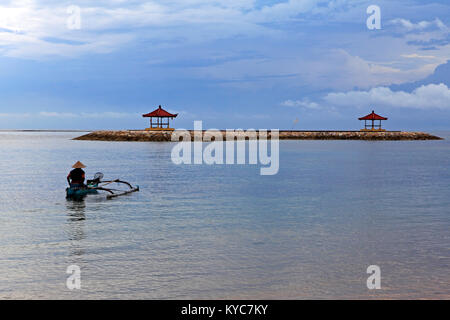 Balinesische Fischer in einem traditionellen Outrigger Holzboot, das Tragen eines kegelförmigen Hut, Paddel in die Lagune am Strand von Sanur vor zwei Pagoden. Bali. Stockfoto