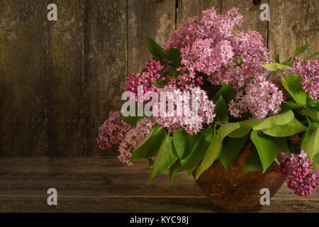 Zusammensetzung mit einem Strauß Flieder in der alten Tontopf auf dem alten Holz- Hintergrund. getönten Foto Stockfoto