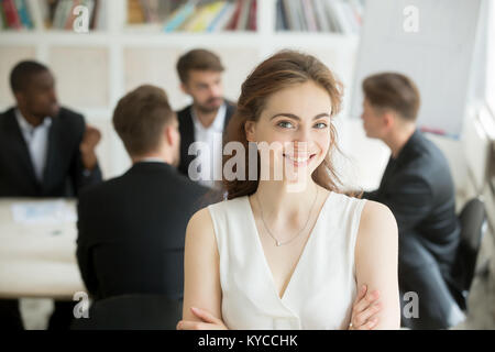 Attraktive weibliche Führer stand mit verschränkten Armen vor männlichen Executive Team Meeting gekreuzt, Lächeln, Geschäftsfrau, Kamera, freundliche Frau b Stockfoto