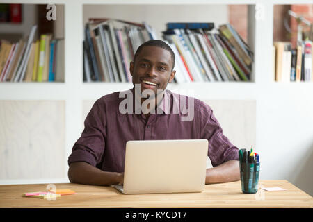 Portrait von freundlich attraktiven afrikanisch-amerikanischen Geschäftsmann Unternehmer am Schreibtisch sitzt mit Laptop Kamera suchen, lächelnd schwarzer Mann business Pr Stockfoto