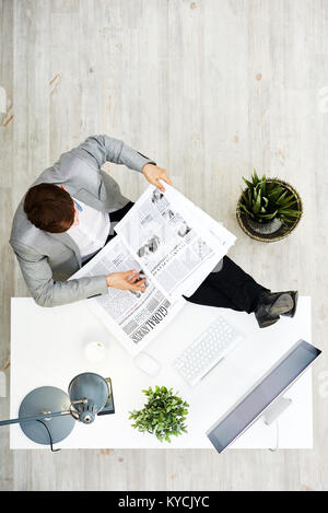 Direkt über der unkenntlich junge Unternehmer mit Interesse lesen Zeitung während der Sitzung mit Beinen auf Büro Schreibtisch Stockfoto