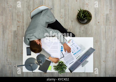 Müde junge weiße Arbeiter unter nap beim Sitzen am Schreibtisch mit Dokumenten behandelt, direkt oberhalb der Ansicht Stockfoto