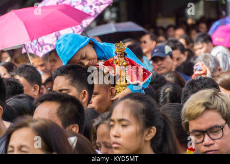 Cebu City, Philippinen. 14. Januar, 2018. Es scheint alle zu viel für dieses kleine Kind hielt seine Santo Nino, halb lächelnd auf seinen Vätern auf seine Schultern Kopf. Als Teil der Sinulog 9 Tag religiöse Fest, der philippinischen Katholiken versammeln sich am frühen Morgen die Sonntagsmesse mit Santo Nino Figürchen, Repliken des Kindes Jesus. Der Glaube in diesem Bildnis stammt aus der Zeit der Entdecker Ferdinand Magellan, der die ursprüngliche Figur als Geschenk, als er im Jahr 1521 bei Cebu landeten gab. Quelle: bildergallerie 2/Alamy leben Nachrichten Stockfoto